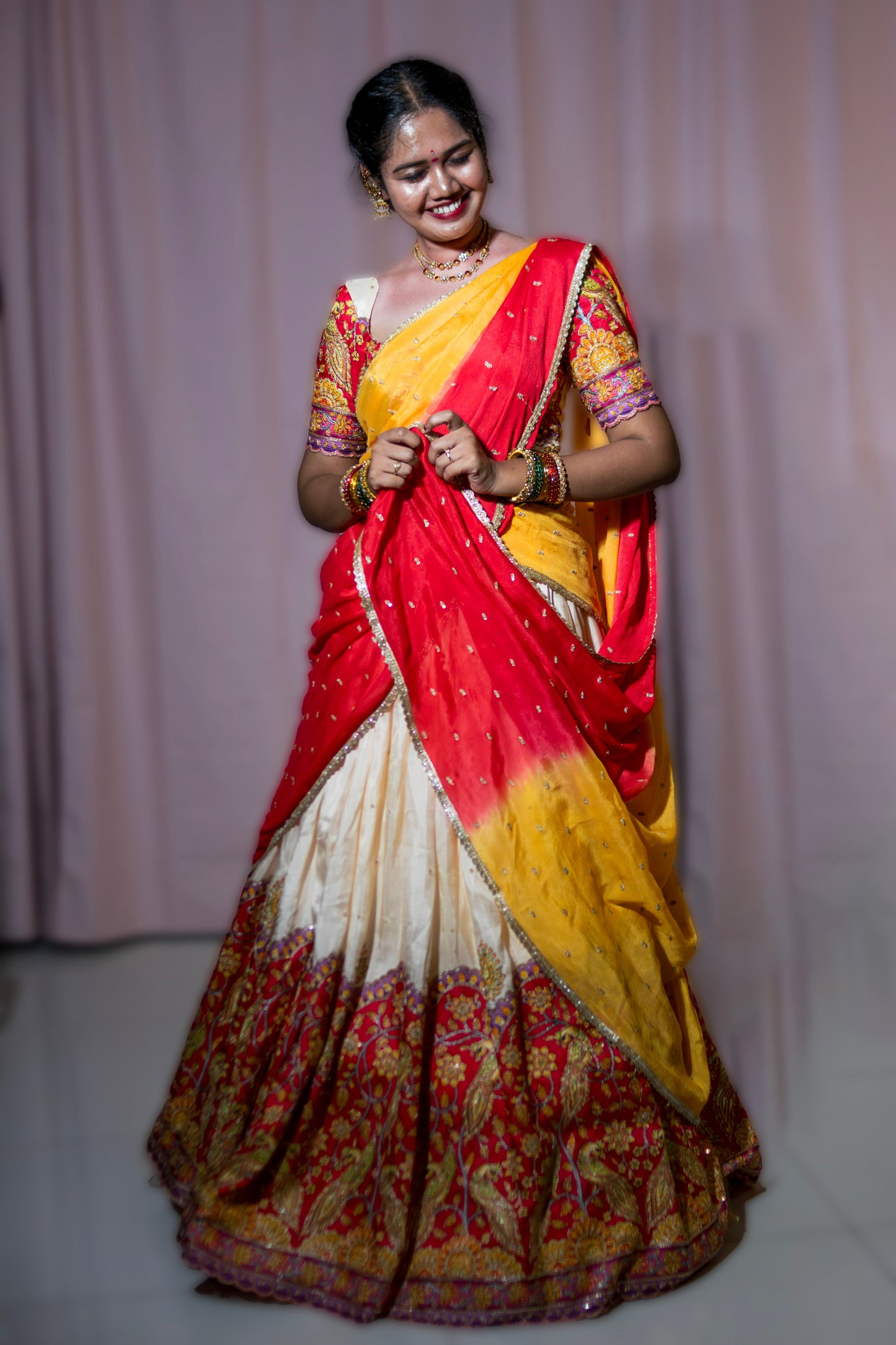 Woman wearing a red, yellow, and white traditional outfit with a floral pattern on a plain background